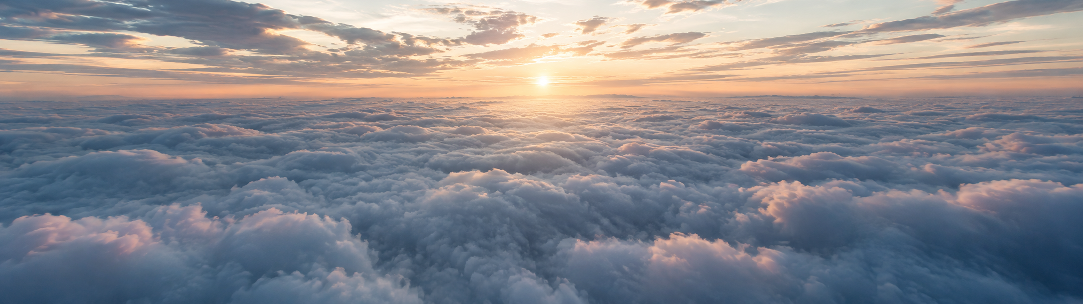 Sun setting on the horizon with a field of clouds in the foreground.